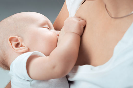 Забавный новорожденный ребенок сосет грудь матери, чтобы питаться грудным молоком